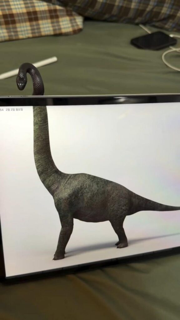 画面から蛇の頭を出す緑色の恐竜が立つ